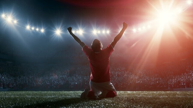 Football player celebrating victory, kneeling on stadium pitch with arms raised under bright lights, cheering crowd