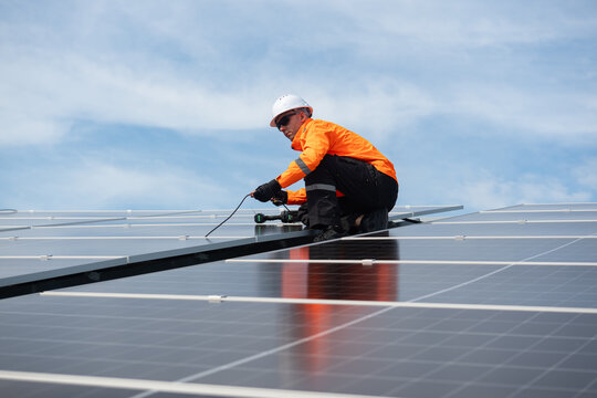 Technician installing solar panels on factory roof for green energy. A skilled technician in safety gear is working on a solar panel installation on rooftop.