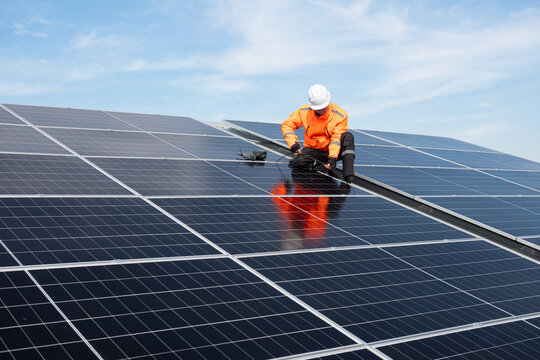 Technician installing solar panels on factory roof for green energy. A skilled technician in safety gear is working on a solar panel installation on rooftop.