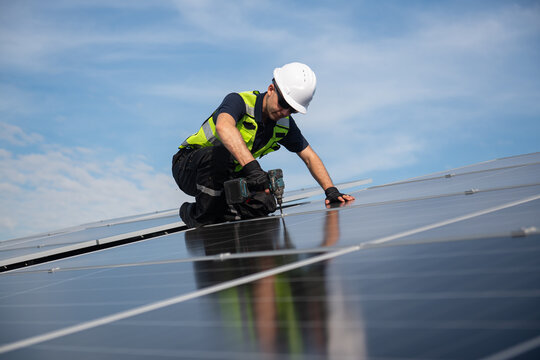 Technician installing solar panels on factory roof for green energy. A skilled technician in safety gear is working on a solar panel installation on rooftop.