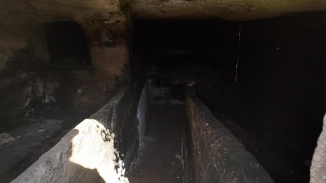 Salina, Malta 06.07.2026 - moving through the entrance into the dark interior of an ancient Paleo-Christian catacomb, revealing carved burial recesses and graves within damp, moss-covered stone walls.