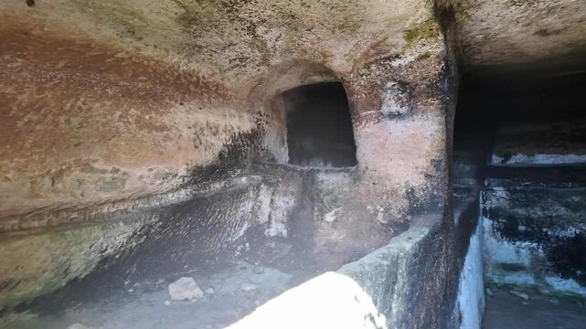 Salina, Malta - the curved interior of an ancient Paleo-Christian catacomb reveals a rock-cut passage with a dark rectangular opening, showcasing centuries of weathering, moss growth, and layered ston