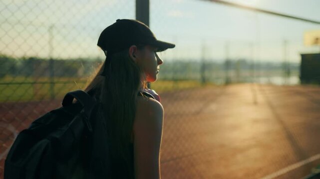 back view, Thoughtful kid walking along chain link fence during golden hour.