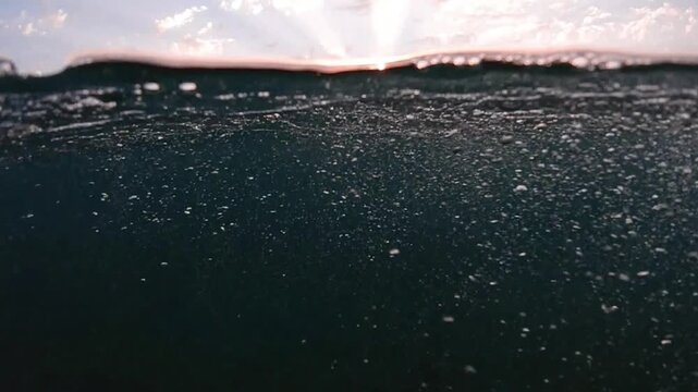 Underwater part and sunset skylight splitted by waterline, underwater bubbles. Beautiful clouds and bright sun over sea water, Real image very suitable for backgrounds in Mediterranean sea, undersea.
