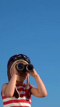 A happy child is playing on a sandy beach. Funny boy pretends to be a sailor during summer vacation. A kid against a background of blue summer sky and sea. Vertical slowmo video