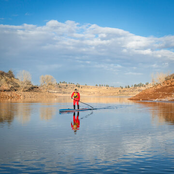 senior male paddler in drysuit is enjoying stand up paddling on lake in Colorado, winter scenery