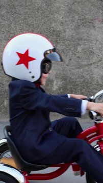 A happy child pretends to be a businessman. Funny kid rides a bike outdoors. A boy has fun during the summer holidays. Back to school, the concept of a business idea. Slow motion, vertical video