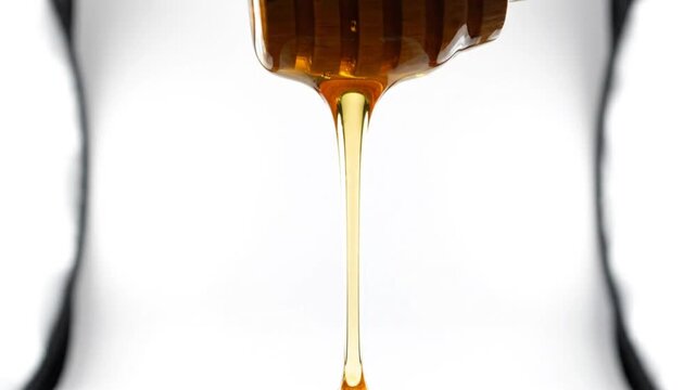 Close-up shot of honey dripping from wooden honey dipper against white background, showcasing sweetness