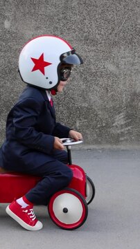 Funny businessman is riding toy car outdoors. Back to school and business concept. Vertical video