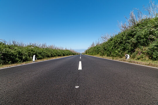Straight empty asphalt road stretching towards the horizon under a clear blue sky in Madeira
