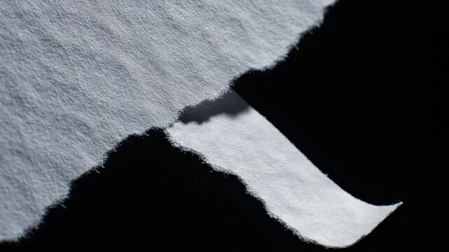 Abstract macro shot of torn paper with jagged edges and deep shadows on a black background creating a minimalist artistic effect