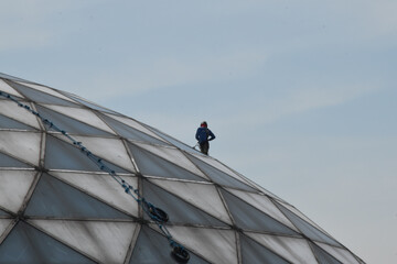A man performing a dangerous job of cleaning a dome made of glass and steel during daytime in a clear day with blue sky. © Nymeria