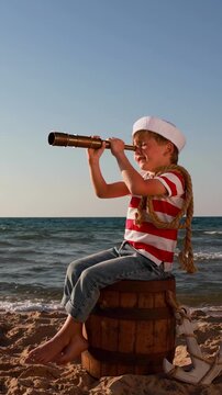 A happy child is playing on a sandy beach. Funny boy pretends to be a sailor during summer vacation. A kid against a background of blue summer sky and sea. Vertical video