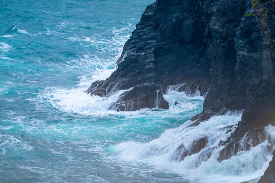 Dramatic view of powerful turquoise ocean waves crashing against dark steep cliffs