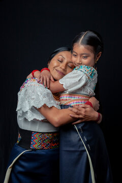 Indigenous Kichwa mother and daughter from Otavalo, Ecuador, wearing traditional hand-embroidered blouses and anaco sharing affectionate moments of cultural heritage in a studio portrait