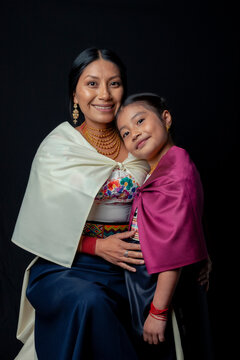Indigenous Kichwa mother and daughter from Otavalo, Ecuador, wearing traditional hand-embroidered blouses and anaco sharing affectionate moments of cultural heritage in a studio portrait