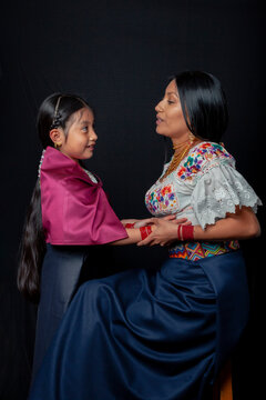 Indigenous Kichwa mother and daughter from Otavalo, Ecuador, wearing traditional hand-embroidered blouses and anaco sharing affectionate moments of cultural heritage in a studio portrait