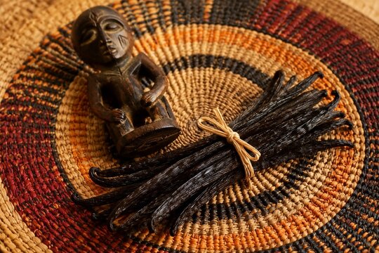 A handwoven raffia table mat with vanilla pods and a wooden carving.