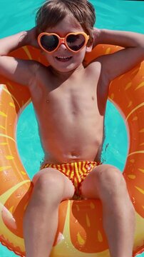 A happy child is having fun on the summer vacation. A kid is swimming in the pool. Vertical video. Slow motion