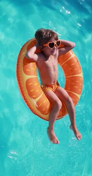 A happy child is having fun on the summer vacation. A kid is swimming in the pool. Vertical video. Slow motion