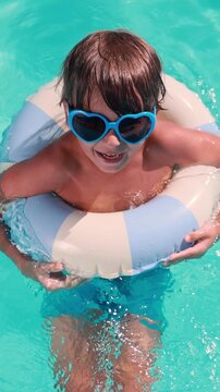 A happy child is having fun on the summer vacation. A kid is swimming in the pool. Vertical video. Slow motion