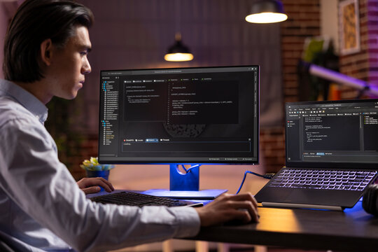 Self employed man sits at desk surrounded with computers, reviewing software and analyzing website structure while young male adult working from home, completing programming tasks during late hours.