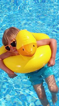 A happy child is having fun on the summer vacation. A kid is swimming in the pool. Vertical video. Slow motion