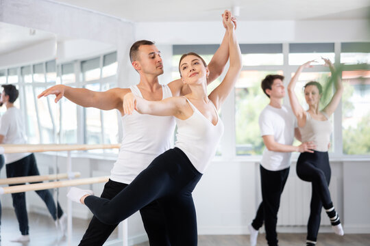 Happy young caucasian man and woman practicing ballet arabesque pose in modern ballroom