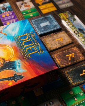 Portrait product photograph of Lord of the Rings Duel for Middle Earth game box and components on wooden table with dramatic lighting designed by Antoine Bauza and Bruno Cathala