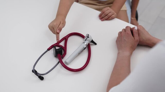 Little child pointing at a stethoscope and otoscope on a pediatrician's desk. Concept child healthcare, curiosity, pediatric medicine, medical examination, learning.