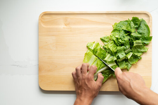 Hands chopping romaine lettuce on cutting board