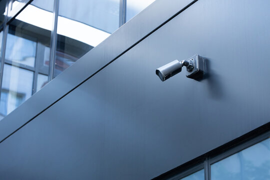 Security camera mounted on a modern building exterior, featuring sleek glass panels and a contemporary architectural design in an urban environment