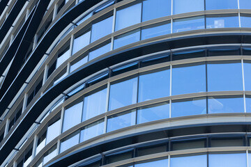 Obraz premium Modern architectural building facade featuring curved glass windows and metal frames, showcasing contemporary design elements in an urban environment