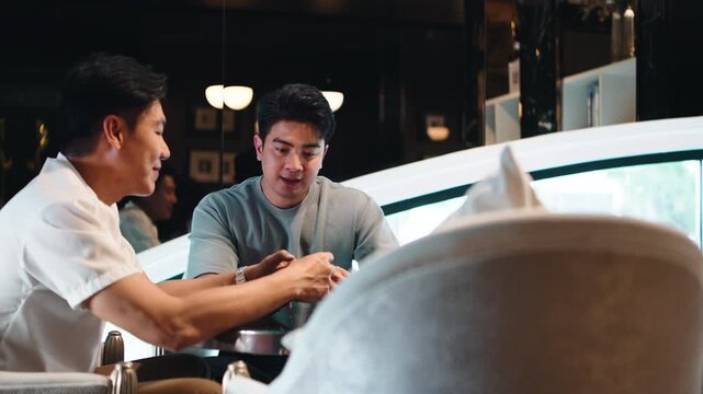 Gay couple laughing and chatting while looking at a smartphone in a cafe