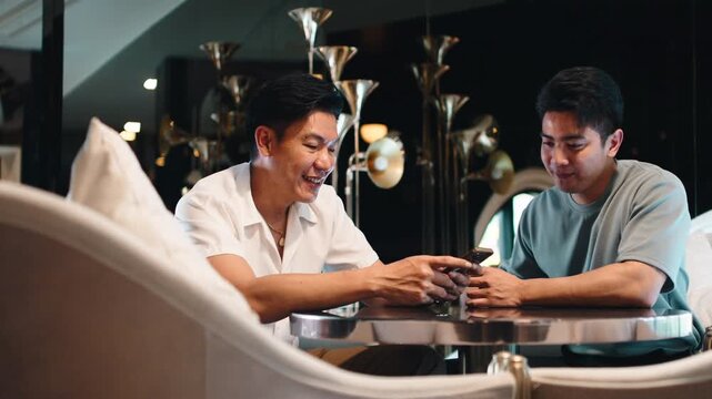 Gay couple laughing together with a smartphone in a luxury hotel lounge