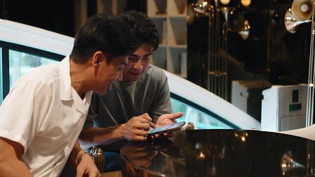 Two male partners happily browsing social media on a phone at a coffee shop