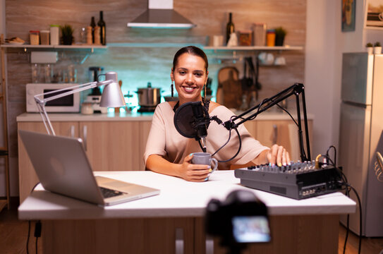 Woman speaks about her life during a podcast in a home studio with neon light, recording online broadcast content, using a microphone setup for online media production.
