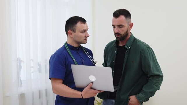Family physician consulting a young man about his health using a laptop in a modern medical clinic. Concept primary healthcare, medical consultation, digital medicine, patient care, healthcare technol