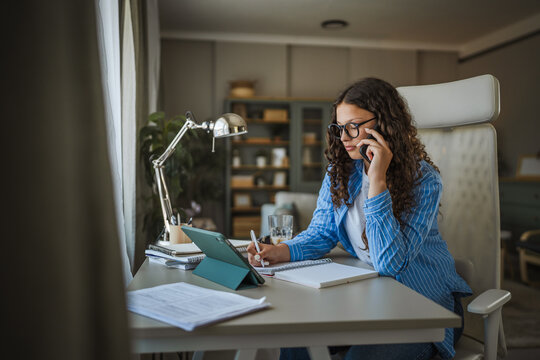 Female freelancer multitasking, working from home office, speaking on phone