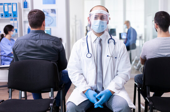 Doctor wearing a protective visor looks toward the camera in a hospital hallway, representing medical staff, safety and clinical work.