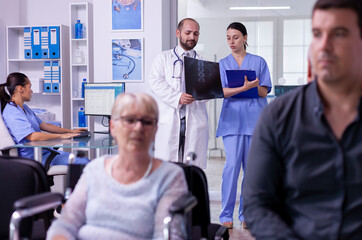 Fototapeta premium Specialist doctor discusses x-ray examination and treatment notes with a nurse while caring for a senior woman in a wheelchair at the hospital.