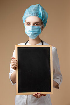 Caucasian Professional Confident Female GP Doctor Posing in Doctor's Smock and Endoscope While Holding Black Board With Empty Space