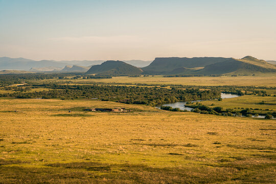 A valley landscape with river meandering through green vegetation. Vast golden steppe meadows stretch to distant hills