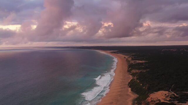 Aerial drone shot of Rio da Prata naturist beach with dramatic clouds and ocean coastline in Sesimbra Portugal. Scenic coastal landscape with waves and sandy shoreline
