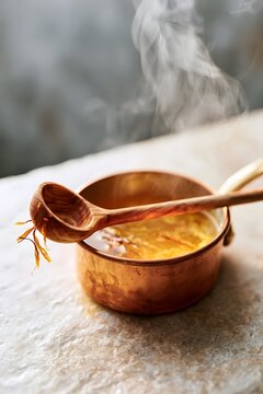 Saffron threads steeping in copper pot with rustic wooden ladle