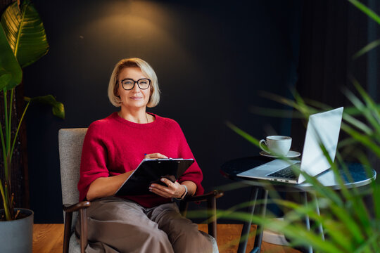 Portrait of 50's stylish, confident mature businesswoman, middle aged experienced senior female professional, business coach, mentor, therapist, counselor working on laptop in office. Female leader