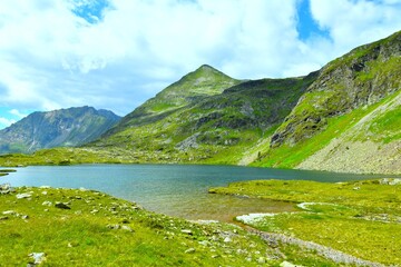 View of Landschitzsee mountain lake bellow gras covered peak and green alpine meadows at the shore in Lungau, Niedere Tauern, Lessachtal, Austria © kato08