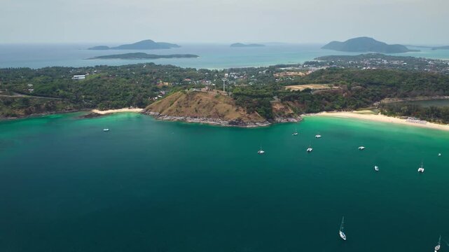 Tropical coastline of Nai Harn Beach in Phuket, Thailand, turquoise sea with yachts anchored near sandy beach and green hills, offering scenic travel and vacation destination. Aerial view drone flight
