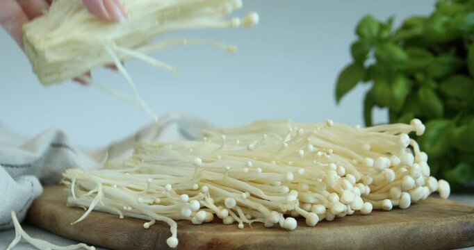 Woman taking raw enoki mushrooms from table, closeup