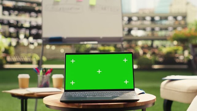 Green screen for chroma key editing with screen replacement on laptop in empty outdoor corporate meeting area rooftop, screen mockup on computer near modern lounge chairs and table.